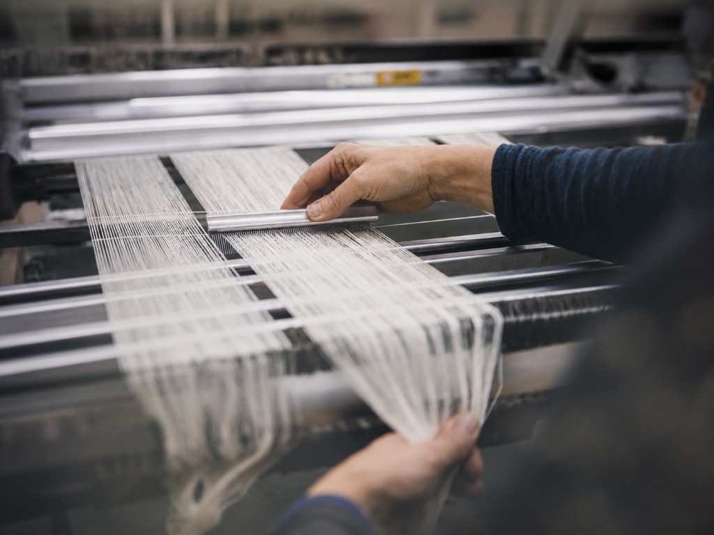 Mani al lavoro su telaio industriale con filati